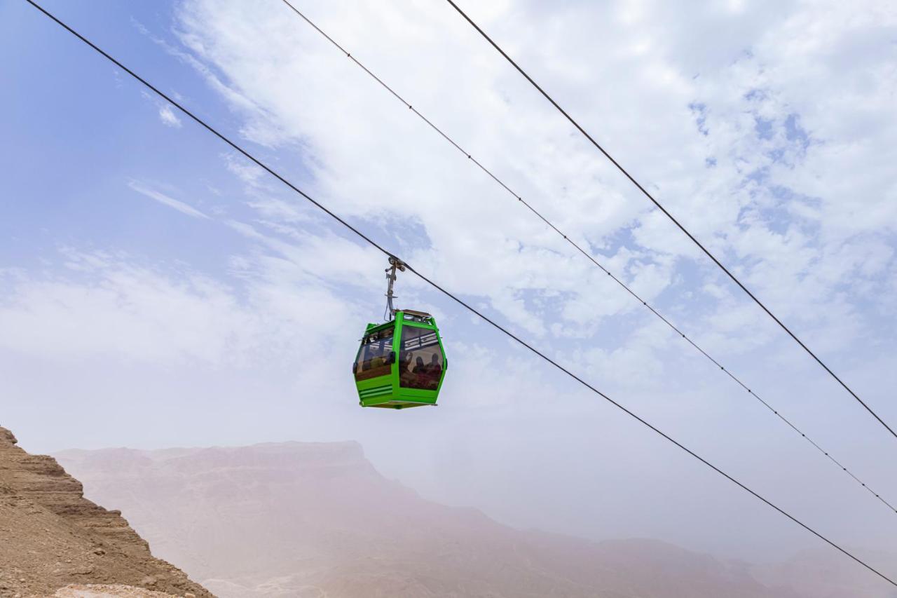 Tolip Resort El Galala Majestic Айн-Сохна Экстерьер фото The photo shows a green cable car suspended in the air, traveling along overhead cables. The backdrop features a hazy landscape, likely mountainous or elevated terrain, with a cloudy sky. The scene suggests a scenic transportation method, possibly us