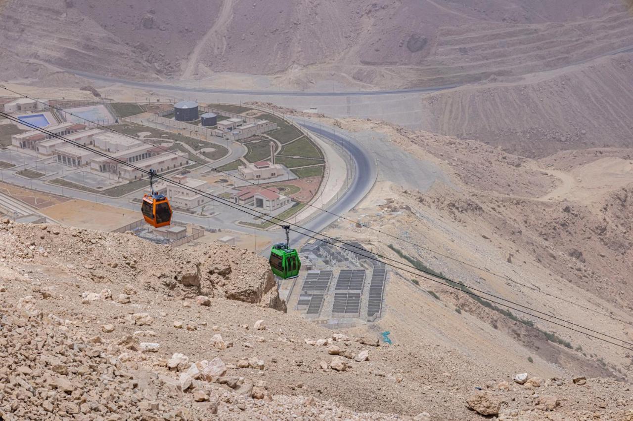 Tolip Resort El Galala Majestic Айн-Сохна Экстерьер фото The photo shows a scenic view from a high elevation, featuring a cable car system. Two cable cars are visible, one orange and one green, traveling along cables down the mountainside. Below, there appears to be a developed area with roads and light st