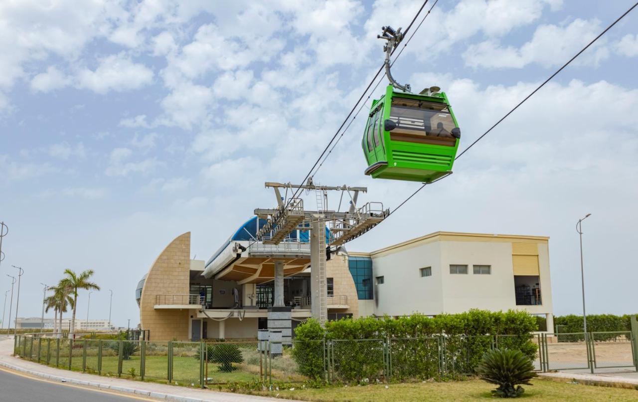 Tolip Resort El Galala Majestic Айн-Сохна Экстерьер фото The photo shows a cable car or gondola system in operation, featuring a green-colored gondola. It is suspended from cables and moving towards a station, which appears to be a modern building with a unique architectural design. The station has large w