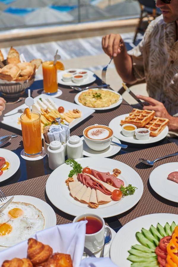 Tolip Resort El Galala Majestic Айн-Сохна Экстерьер фото The photo shows a breakfast spread laid out on a table. There are several plates with a variety of food items, including:

1. **Sliced Cold Cuts**: A plate featuring various cold meats, accompanied by garnishes like cherry tomatoes and lettuce.
2. **