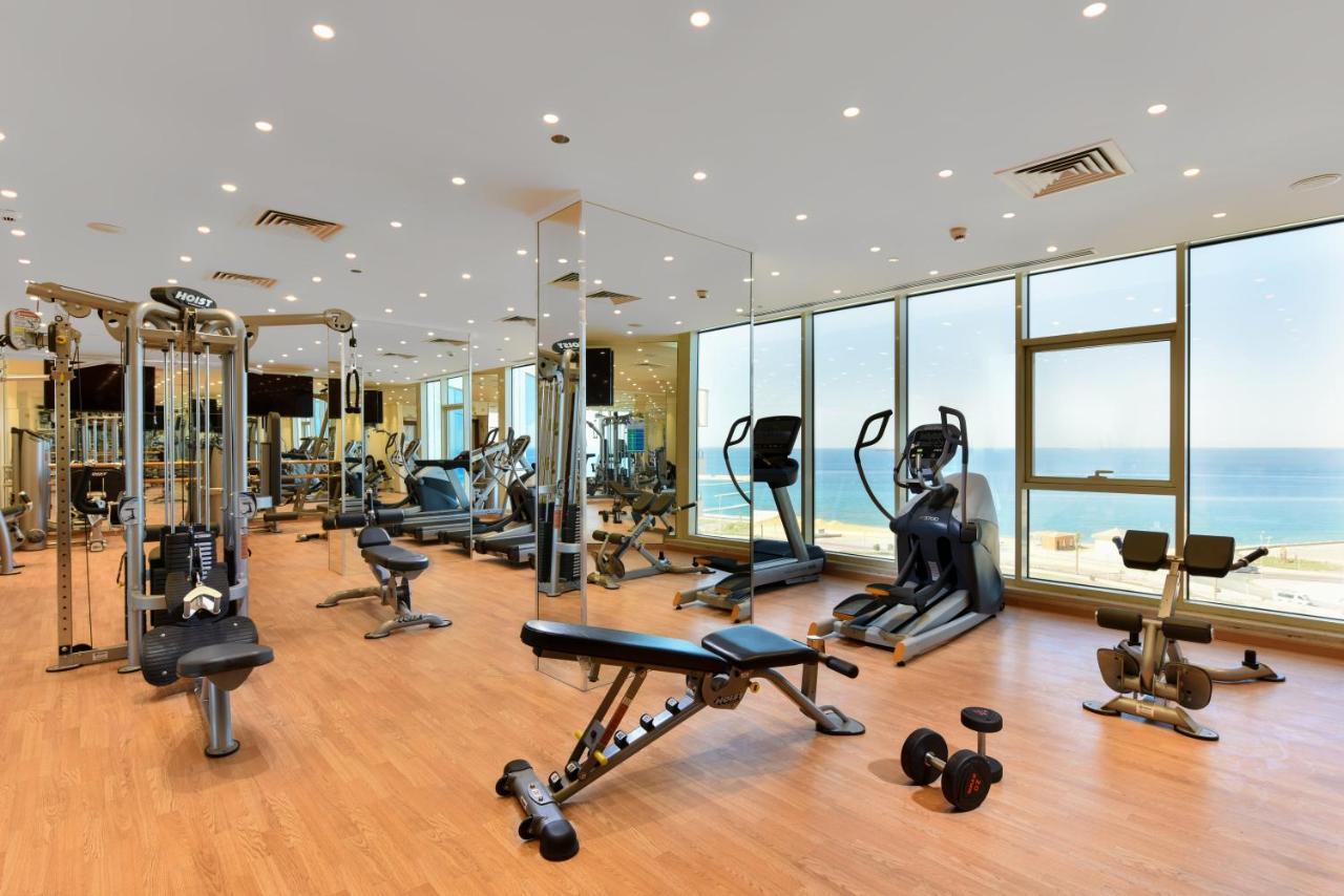 Tolip Resort El Galala Majestic Айн-Сохна Экстерьер фото The photo shows a modern gym interior with a variety of fitness equipment. There are cardio machines like treadmills and ellipticals, along with strength training equipment such as free weights and benches. The gym features large windows that offer a