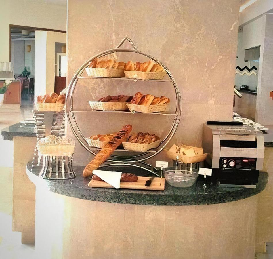 Tolip Resort El Galala Majestic Айн-Сохна Экстерьер фото The photo shows a display of various types of bread and pastries arranged on a countertop. There are several baskets stacked on a circular stand, filled with different baked goods like croissants and rolls. A long baguette is placed horizontally on a